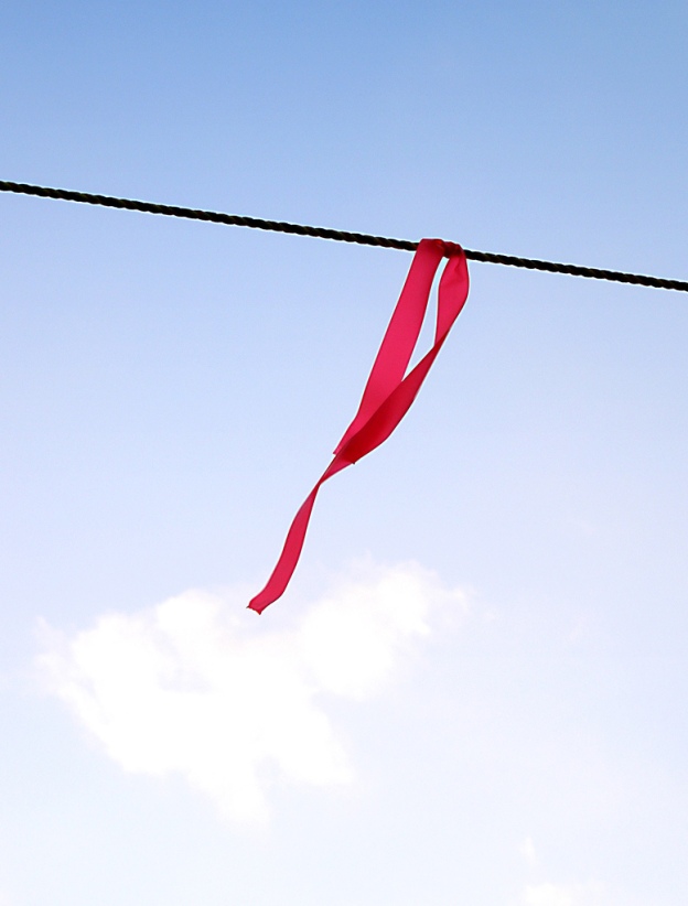 Photo of a single pink ribbon tied around a wire, shot against the sky by tanakawho